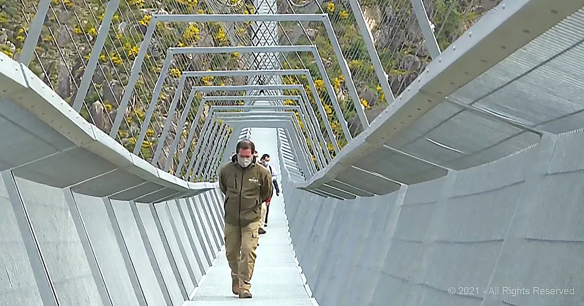 A man in a brown jacket walks through a modern, geometrically designed pedestrian bridge.