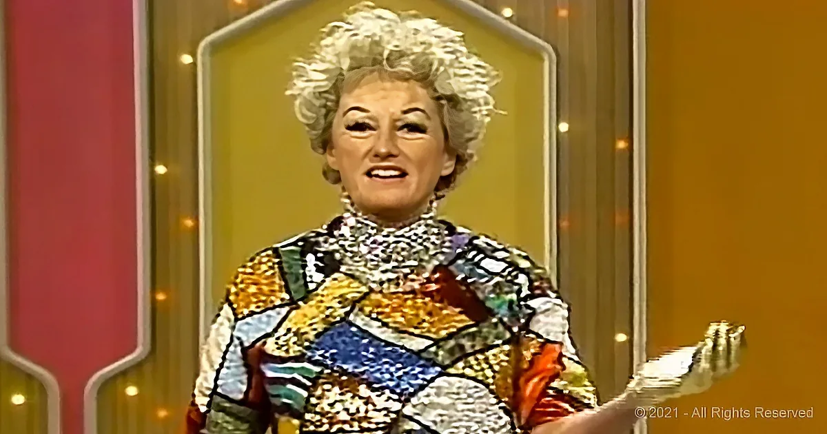 A woman with curly hair, wearing a colorful, patterned dress, stands in front of a vibrant, decorative background.