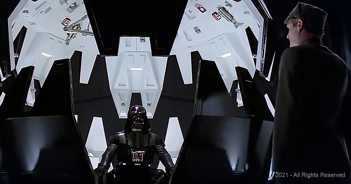 Darth Vader stands in front of a large, futuristic, white, and black structure, facing a man in a dark uniform.