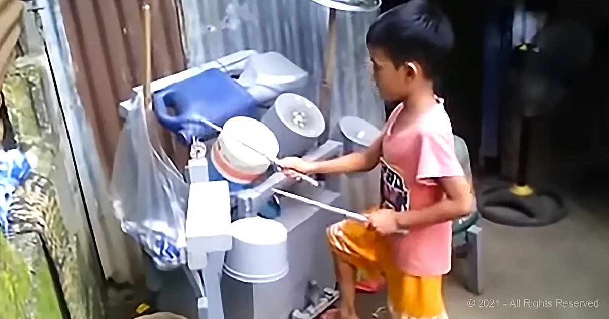 A child in a pink shirt is cooking on a stove with pots and pans, surrounded by household items.