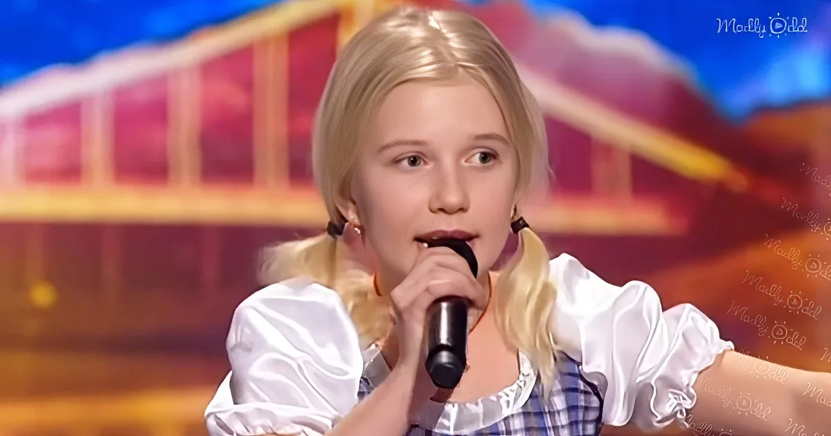A young girl with blonde hair in pigtails sings into a microphone on a stage with a colorful background.