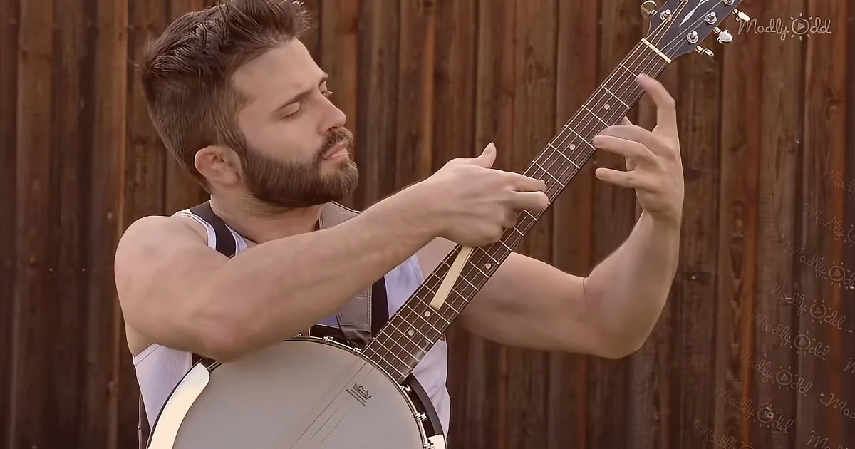 A man with a beard plays a banjo, focusing intently on the strings.