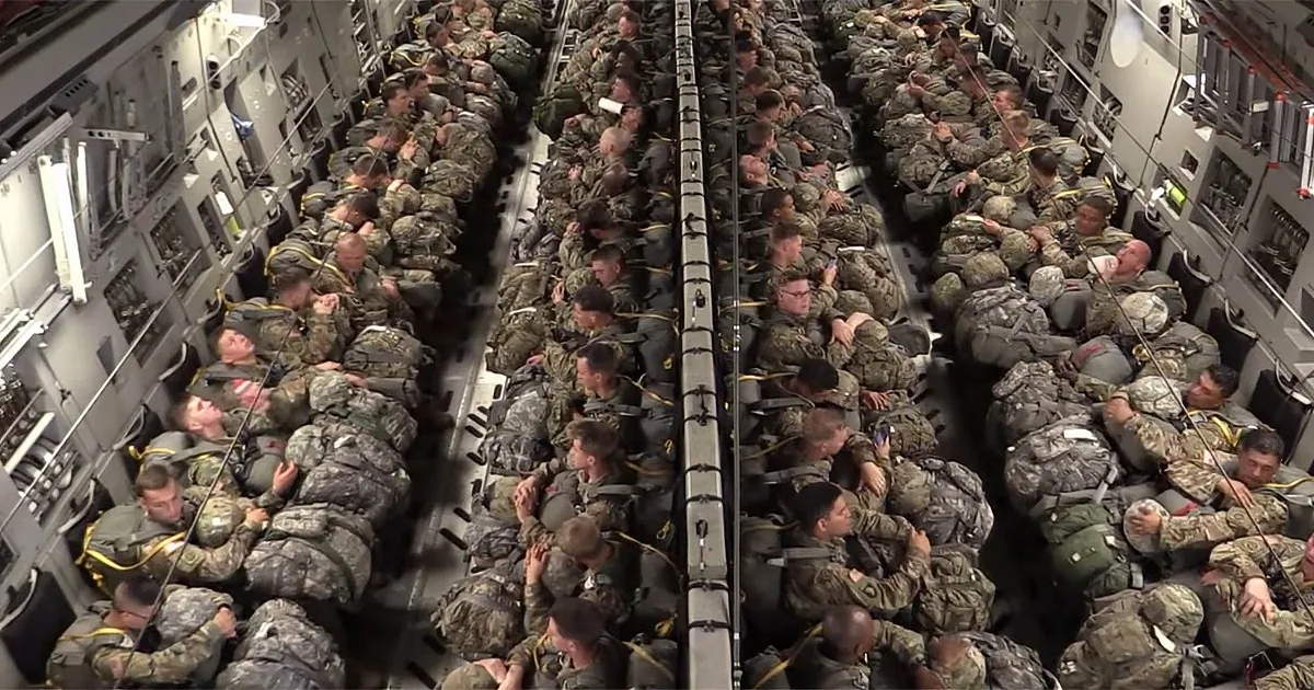 Soldiers in camouflage gear are tightly packed inside a military transport aircraft.
