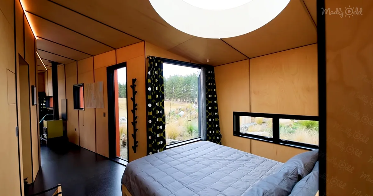 A cozy bedroom with a bed, large windows, and a circular skylight, offering a serene outdoor view.