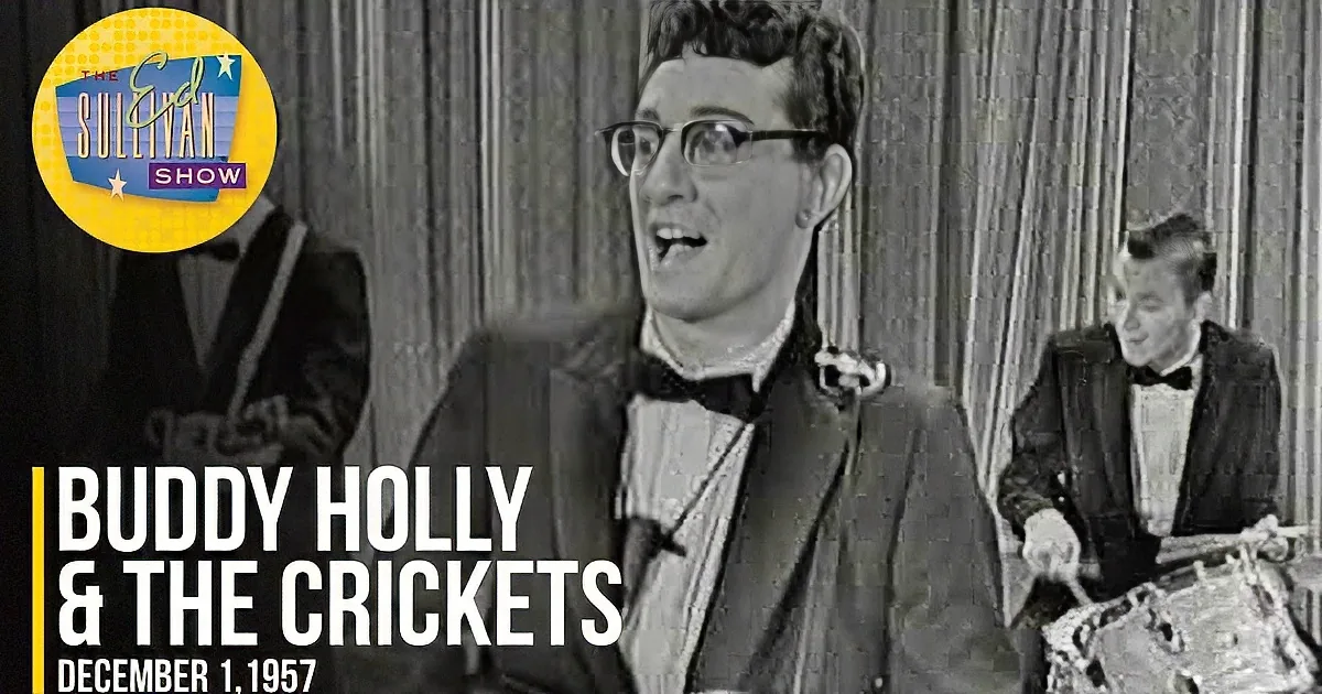 A man in a suit and bow tie sings passionately, accompanied by musicians playing guitars.