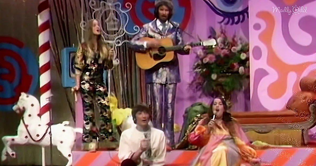 A man in a colorful suit plays guitar on stage with a woman singing beside him.