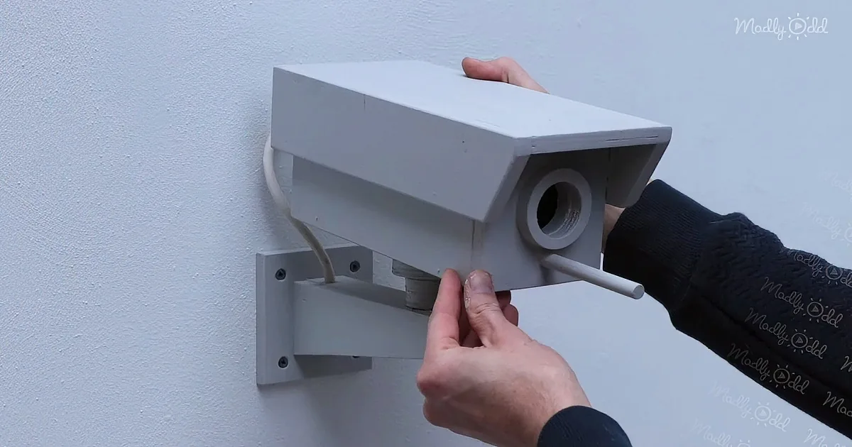 A person is adjusting a white security camera mounted on a wall.