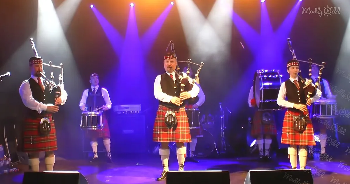 A group of bagpipers in kilts perform on stage under colorful lights.