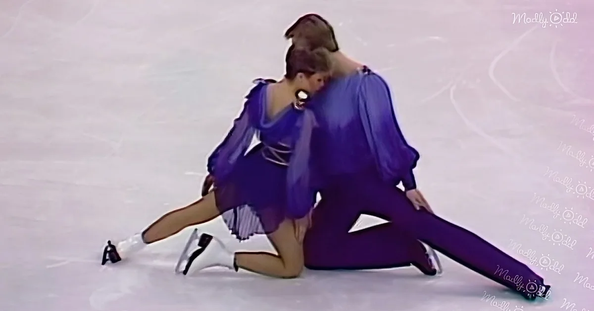 Two figure skaters in purple costumes perform a dramatic pose on the ice.
