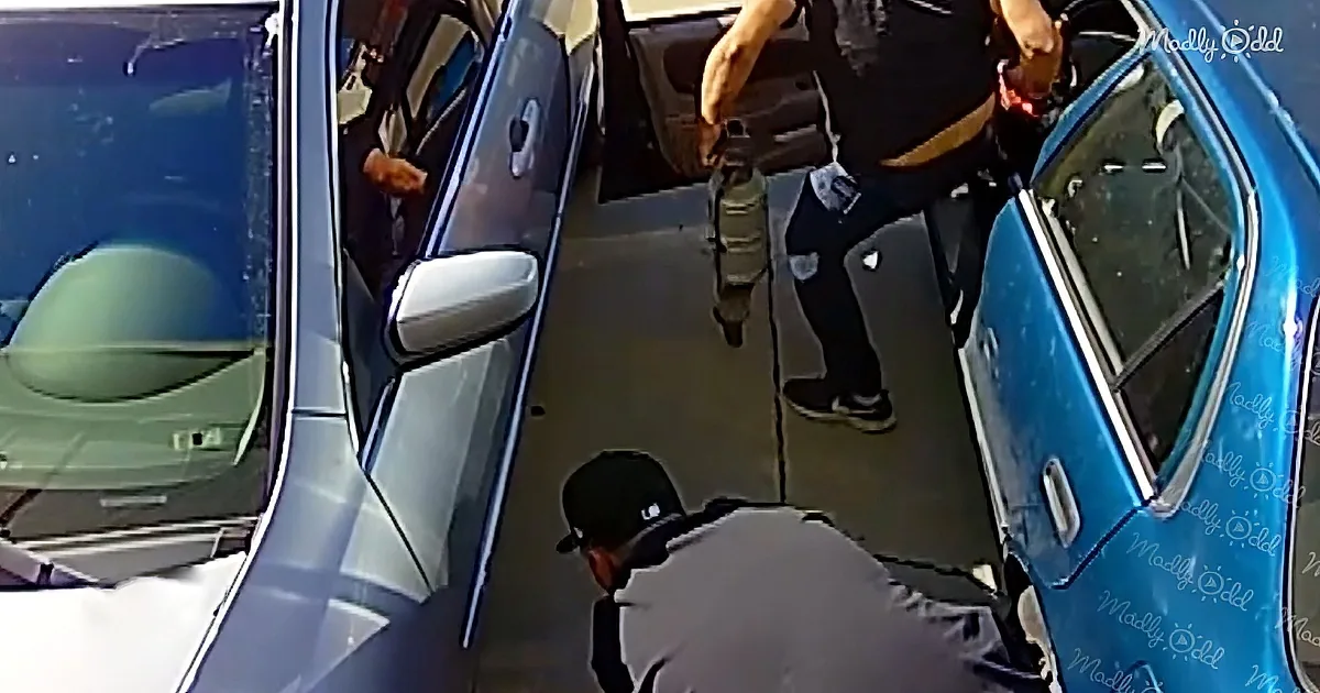 A man in a black shirt and pants holds a tool, while another man in a cap bends over near a blue car door.