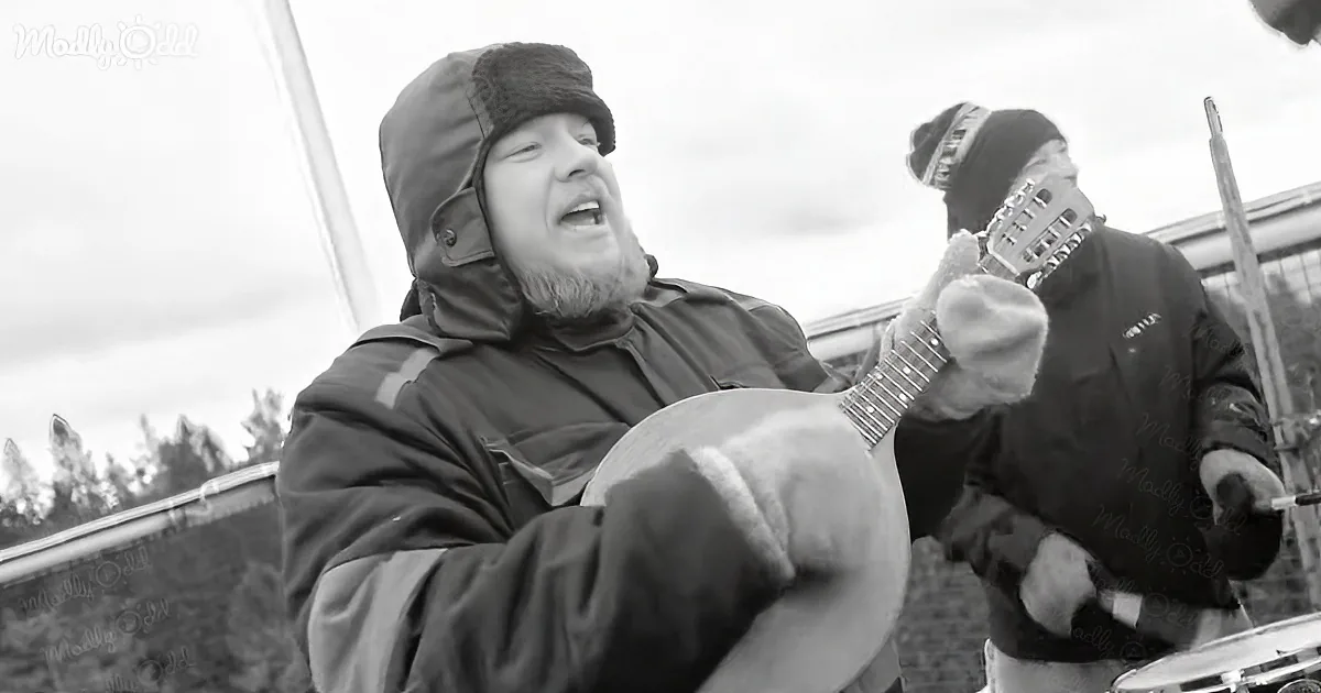 A man in winter gear plays a guitar outdoors, singing passionately.
