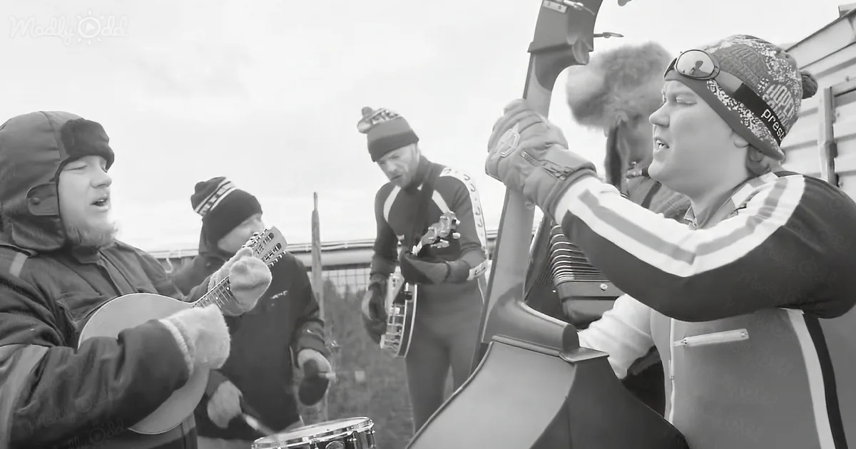 A person in a beanie and gloves plays a large stringed instrument while others sing and play guitars in the background.