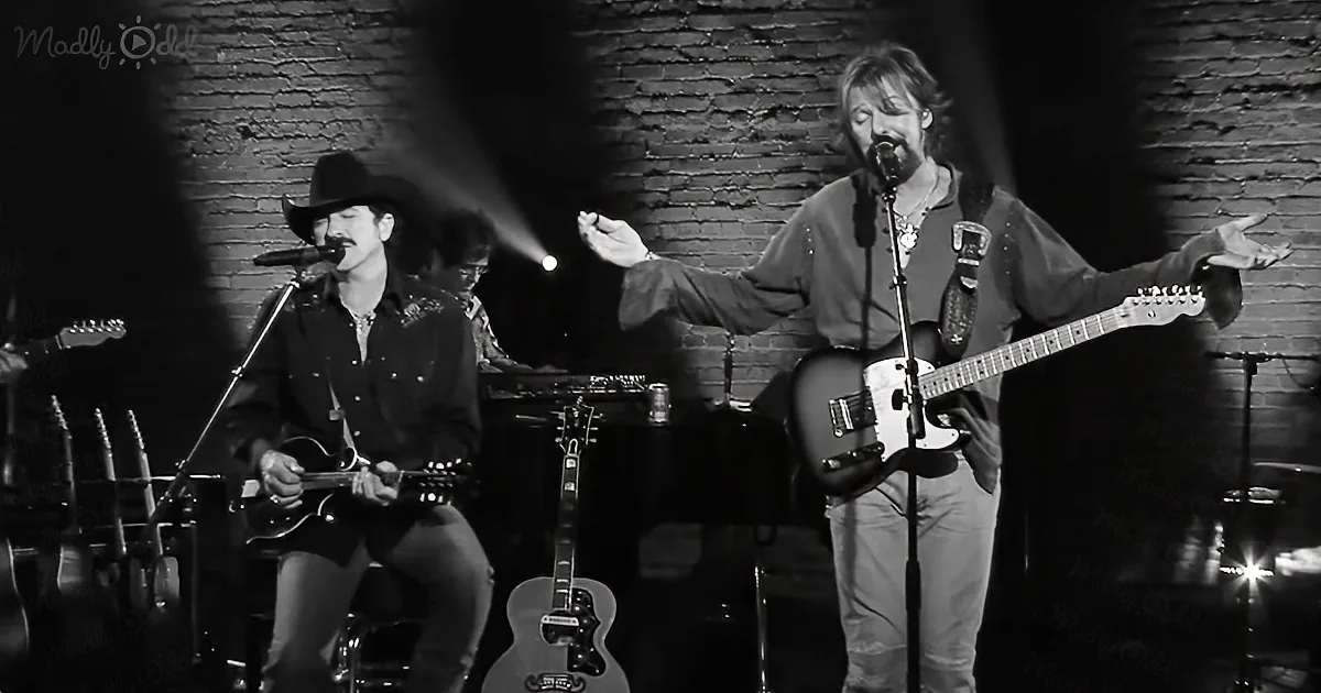A musician in a cowboy hat plays guitar while another gestures dramatically on stage.