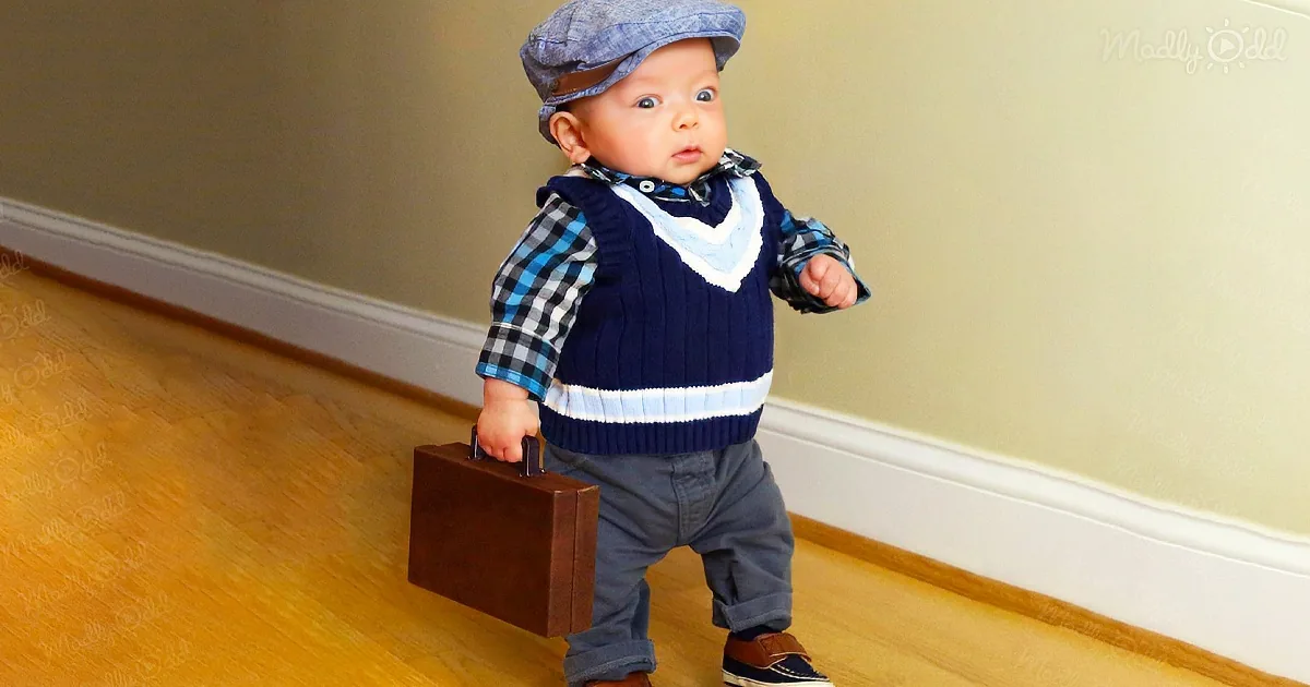 A baby dressed in a blue outfit and hat carries a small suitcase, standing on a wooden floor.