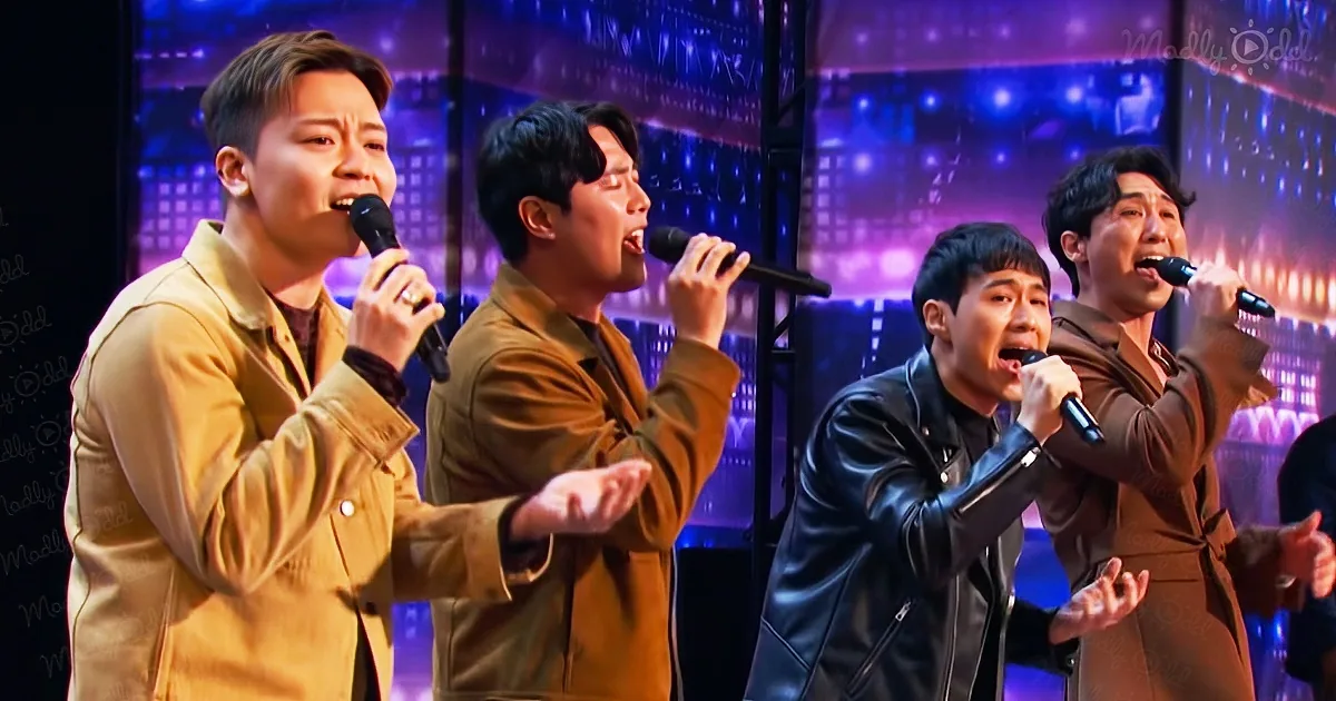 Four men in brown jackets sing into microphones on a stage with colorful lights.