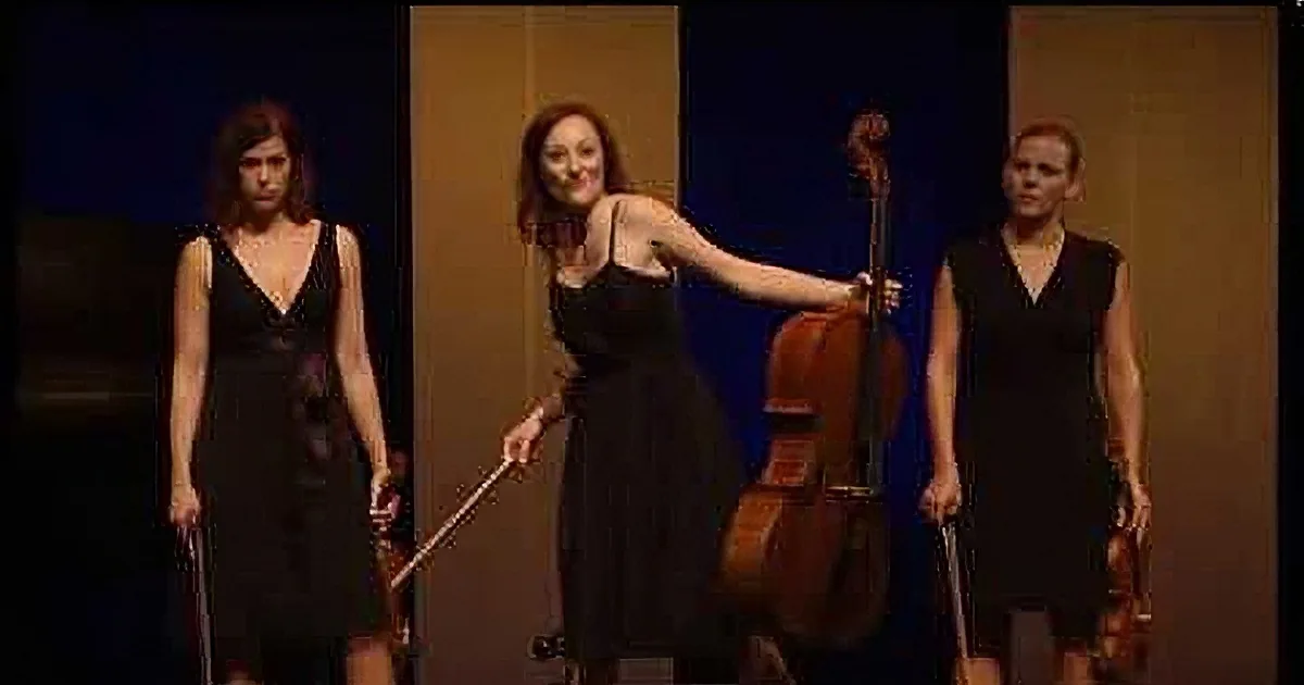 Four women in black dresses perform a synchronized pose with musical instruments on stage.