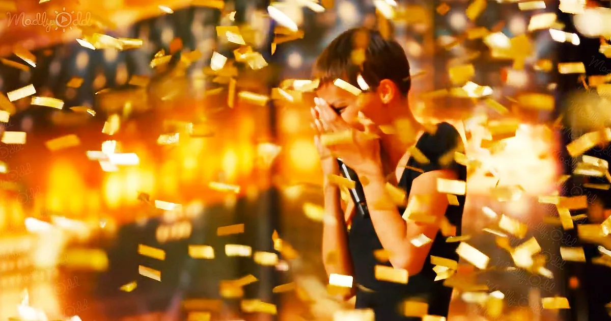 A person in a black dress stands amidst golden confetti, covering their face with their hands.