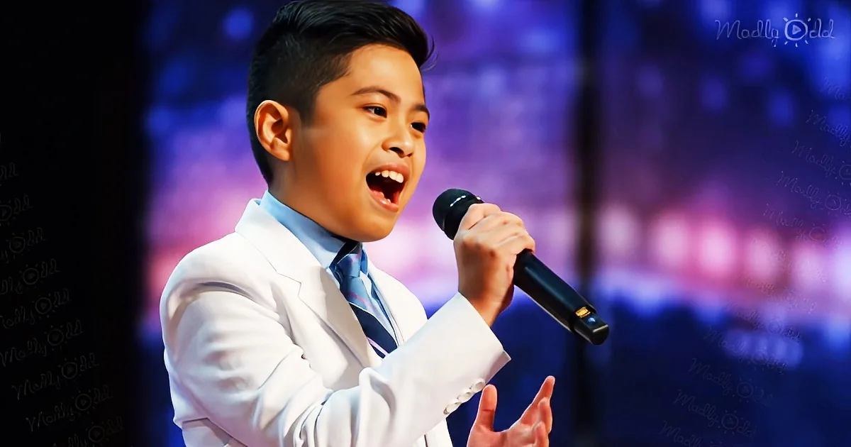 A young boy in a white suit sings passionately into a microphone on stage.