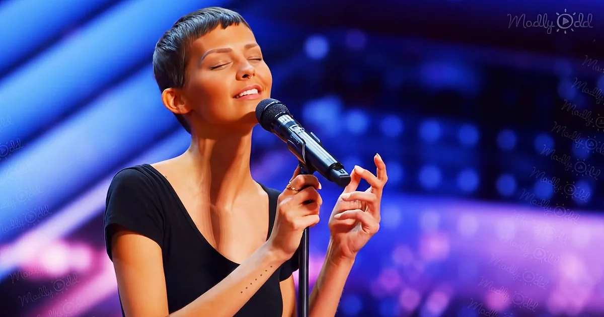 A woman with short hair sings passionately into a microphone on stage.