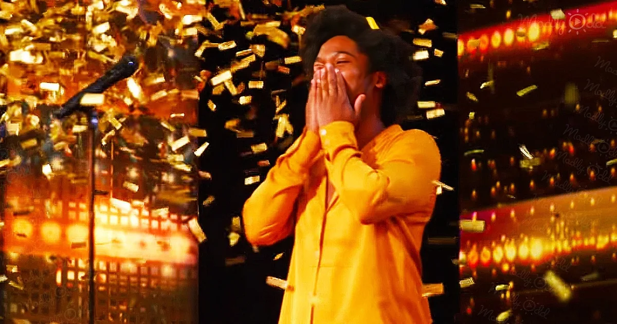 A person in a yellow suit covers their face with their hands amidst falling confetti and vibrant stage lighting.