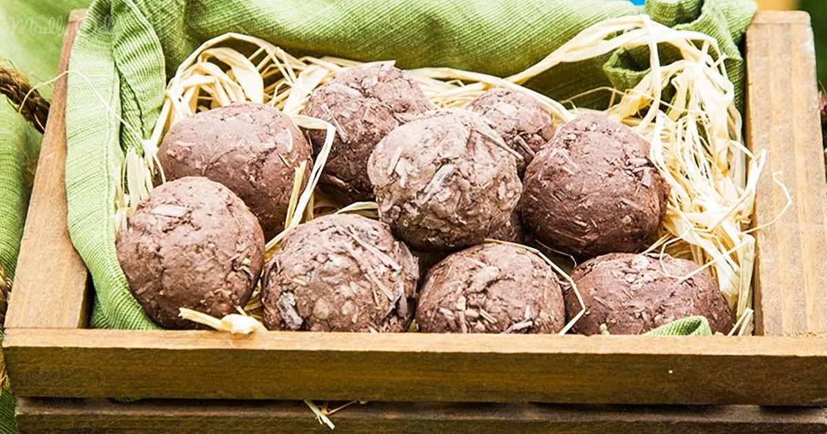 Chocolate truffles in a wooden crate lined with straw and a green cloth.