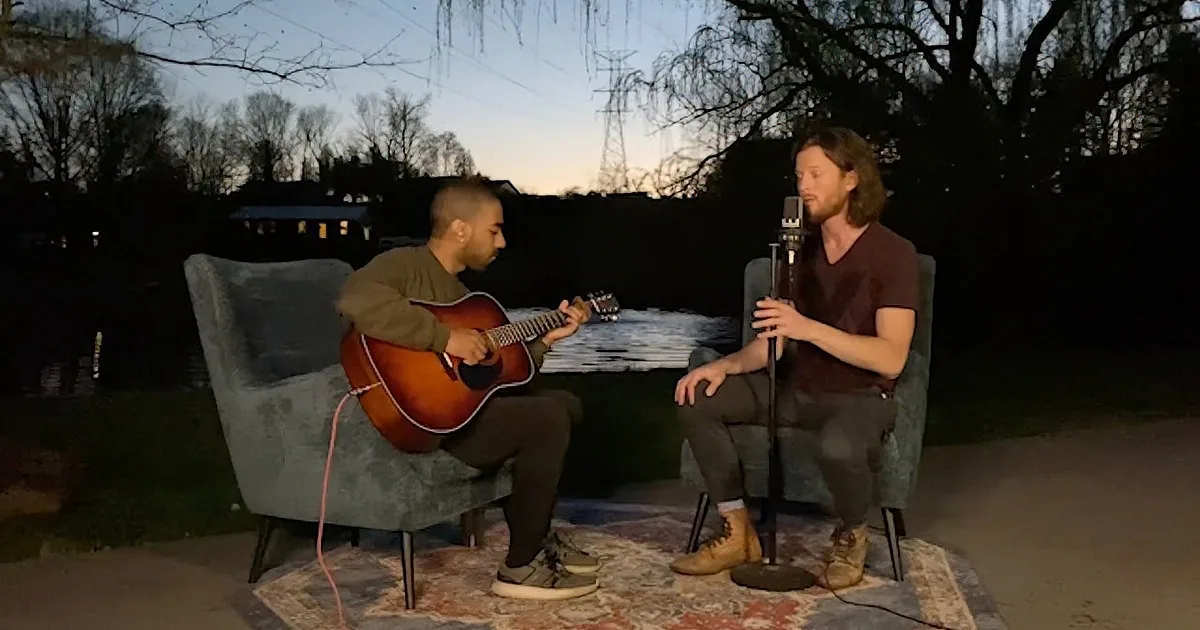 Two men are performing outdoors, one playing guitar and the other singing into a microphone.