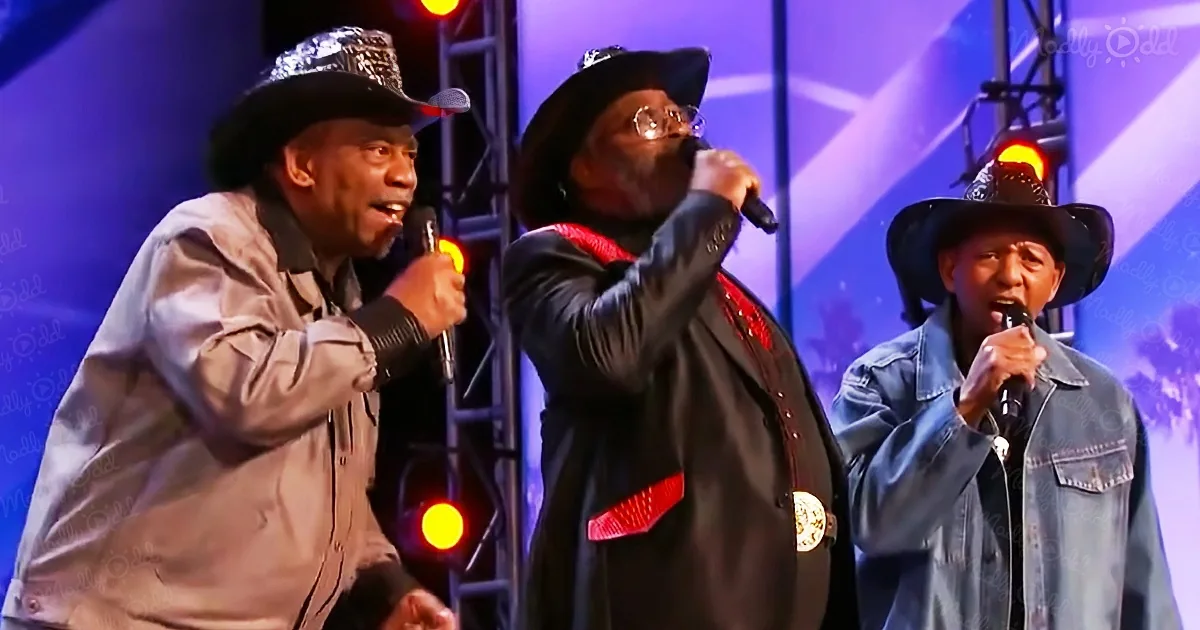 Three men in cowboy hats sing into microphones on a stage with colorful lights.