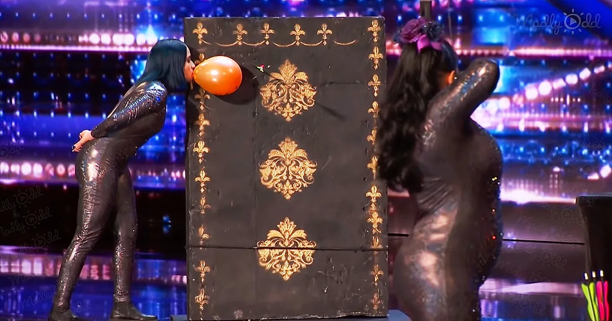 Two people in shiny outfits interact with a large, ornate door on a stage.