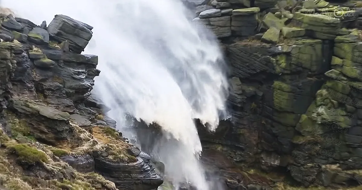 A powerful waterfall cascades down a rugged, moss-covered cliff face.