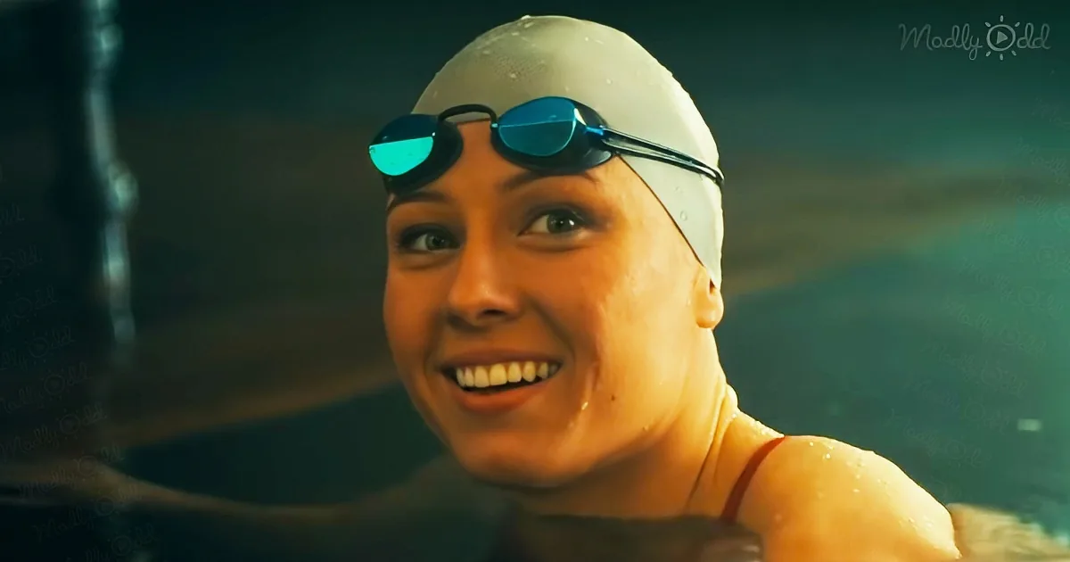 A swimmer wearing a white cap and goggles smiles while in water, with a dark background.