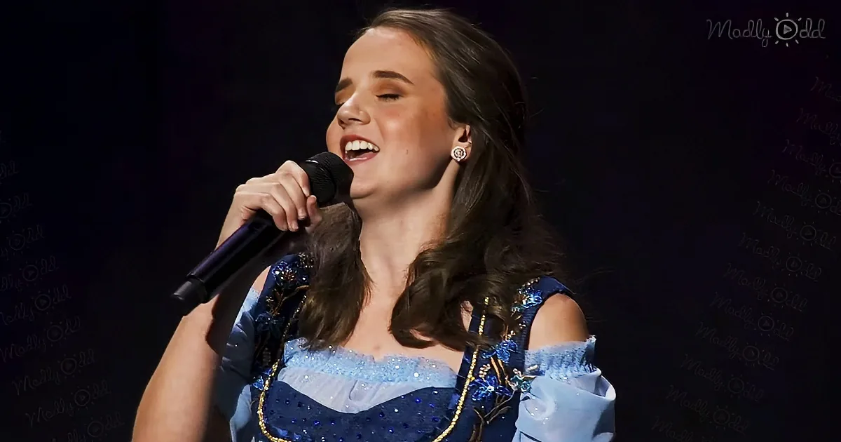 A woman in a blue, sparkly dress sings into a microphone on stage.