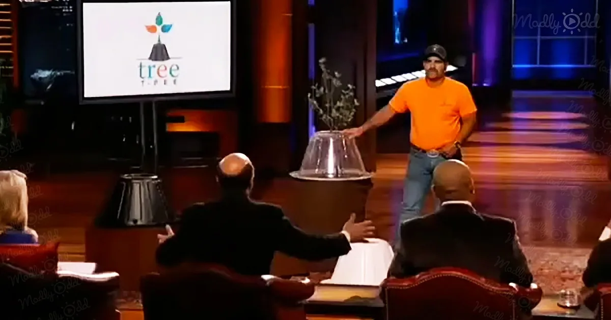 A man in an orange shirt stands on a stage, presenting a product to investors.