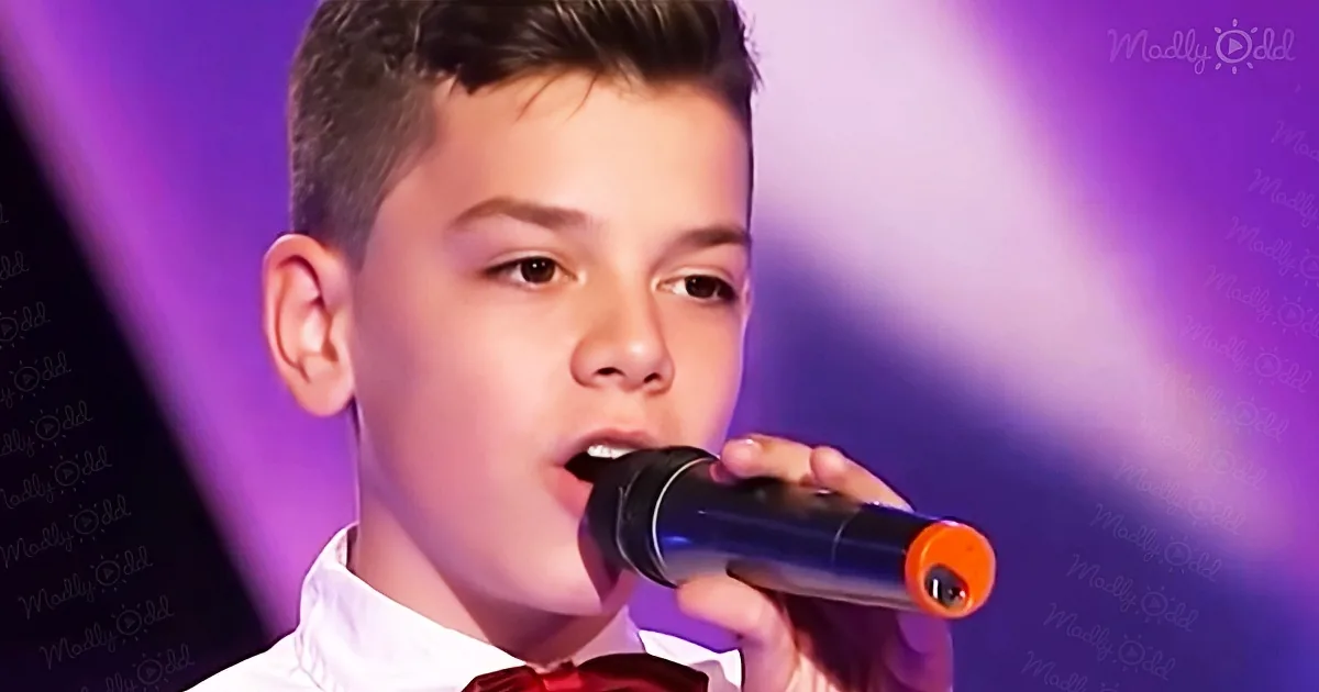 A young boy in a white shirt and red bow tie sings into a microphone, with a purple background and "Madly Odd" text.