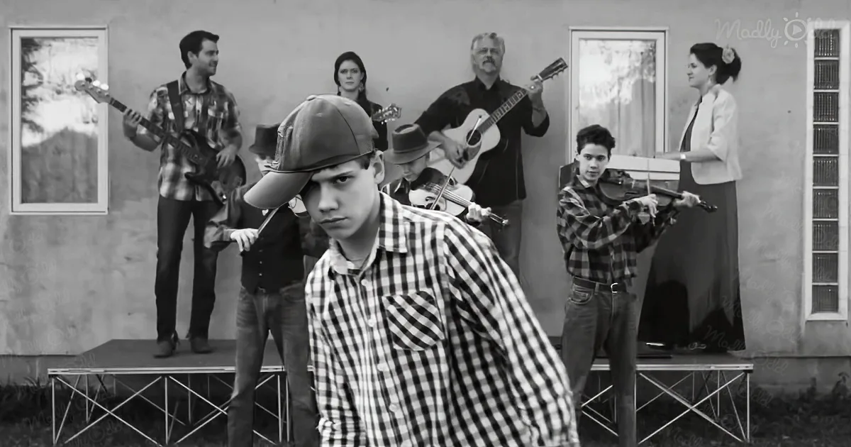 A young boy in a checkered shirt and cap stands in the foreground, with a band playing behind him on a stage.
