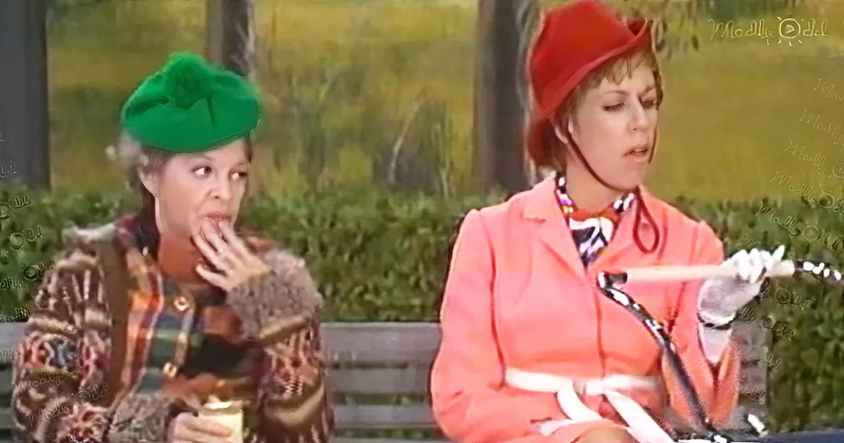 A woman in a green beret and patterned coat sits on a bench, holding a drink, while another woman in a red hat and pink...