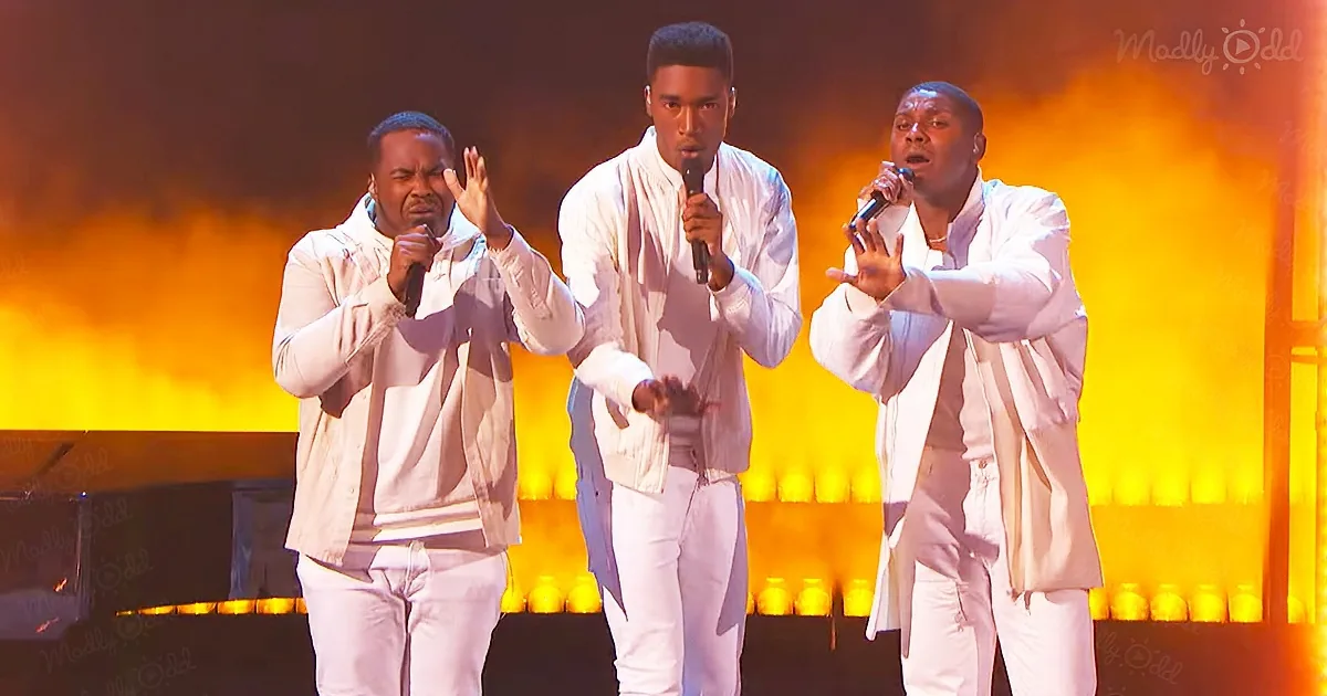 Three men in white perform on stage with microphones, illuminated by vibrant orange and yellow lights.