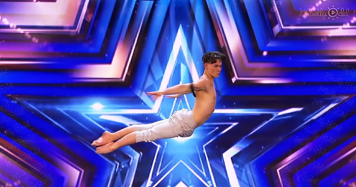 A shirtless man performs an acrobatic move on a stage with a star-shaped background.