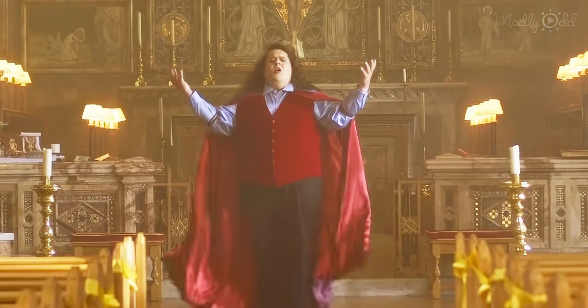 A person in a red cape stands with arms raised in a grand, ornate room with candles and intricate decorations.
