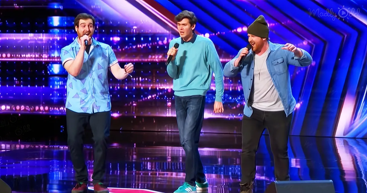 Three men on stage with microphones, performing in front of a colorful backdrop.