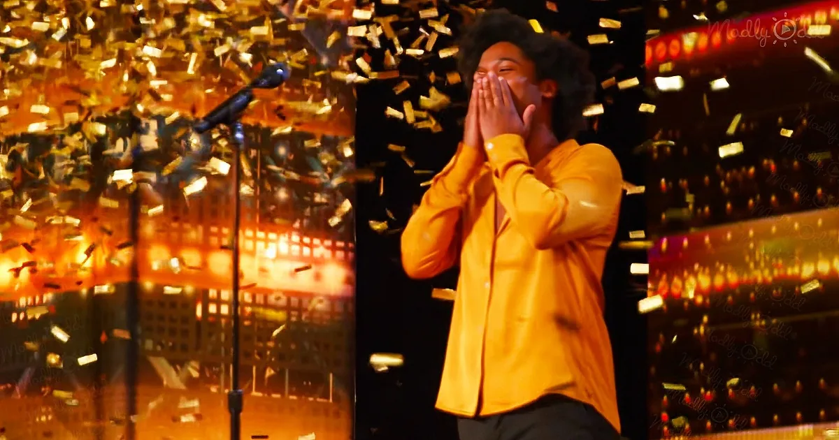 A person in a yellow shirt covers their face with their hands amidst falling confetti and stage lights.