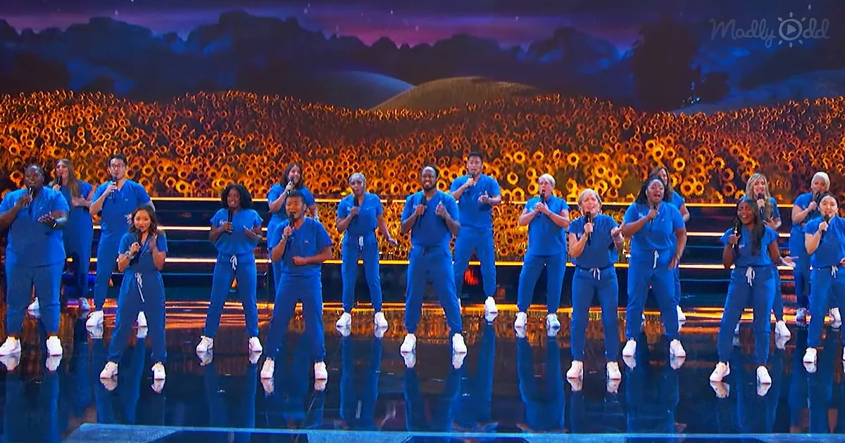A group of people in blue scrubs perform on stage with a vibrant background.