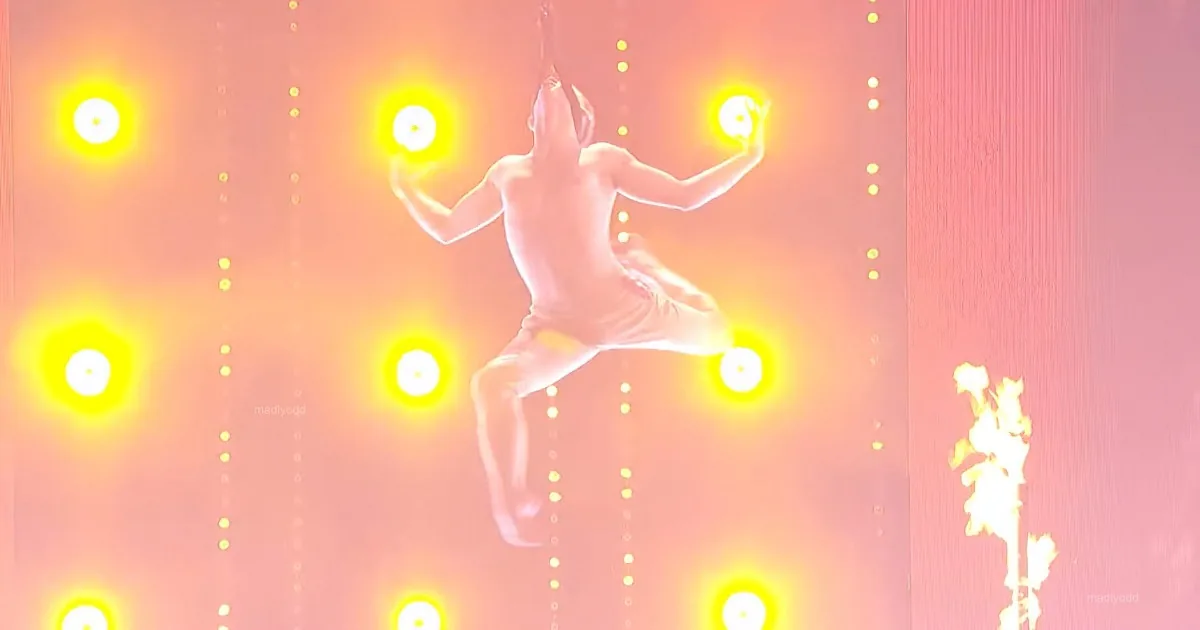 A person is suspended in mid-air, surrounded by glowing yellow lights against a pink background.