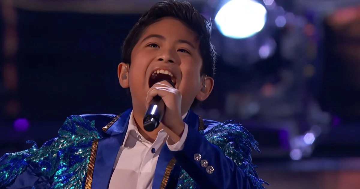 A young boy in a blue sequined jacket sings passionately into a microphone on stage.