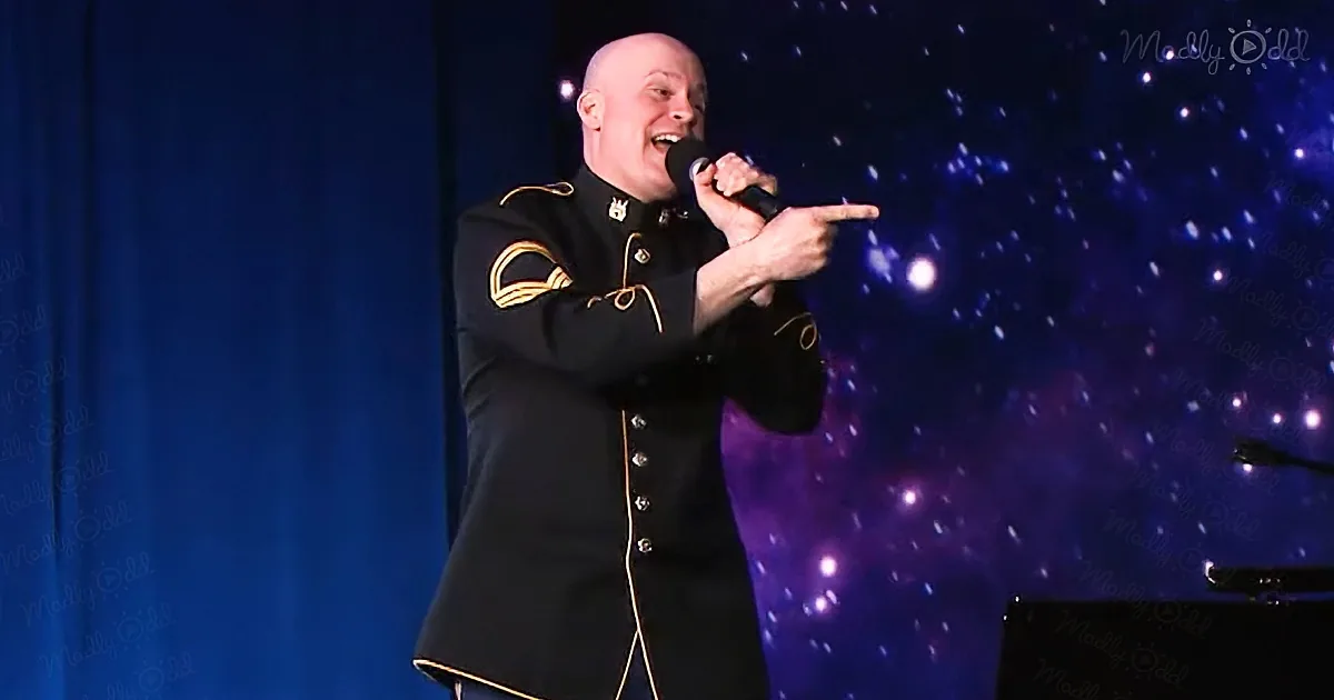 A man in a military uniform sings into a microphone on stage with a starry backdrop.