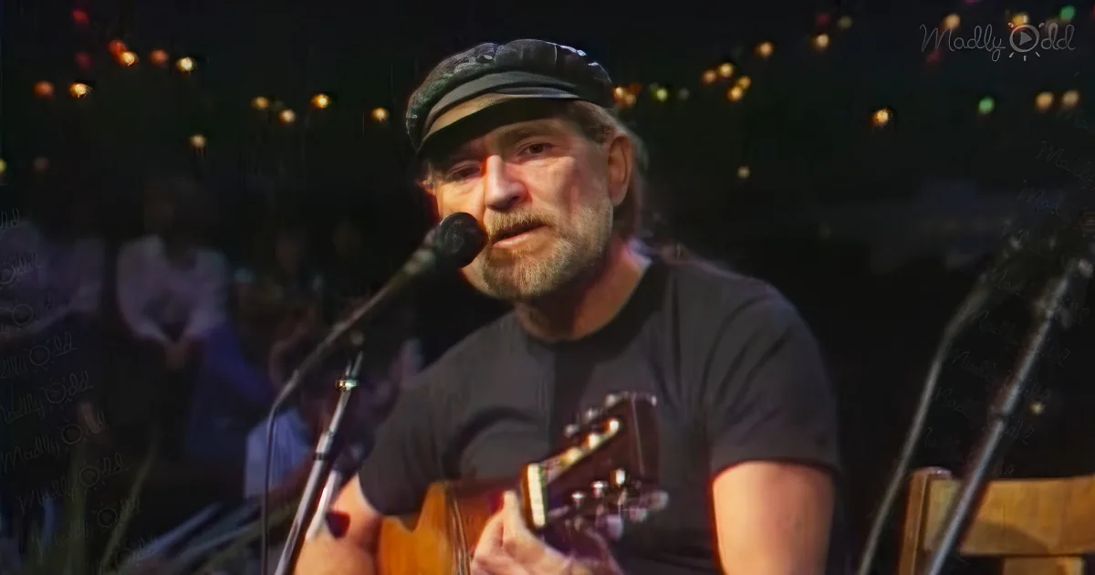 A man with a beard and hat sings into a microphone while playing guitar on stage.