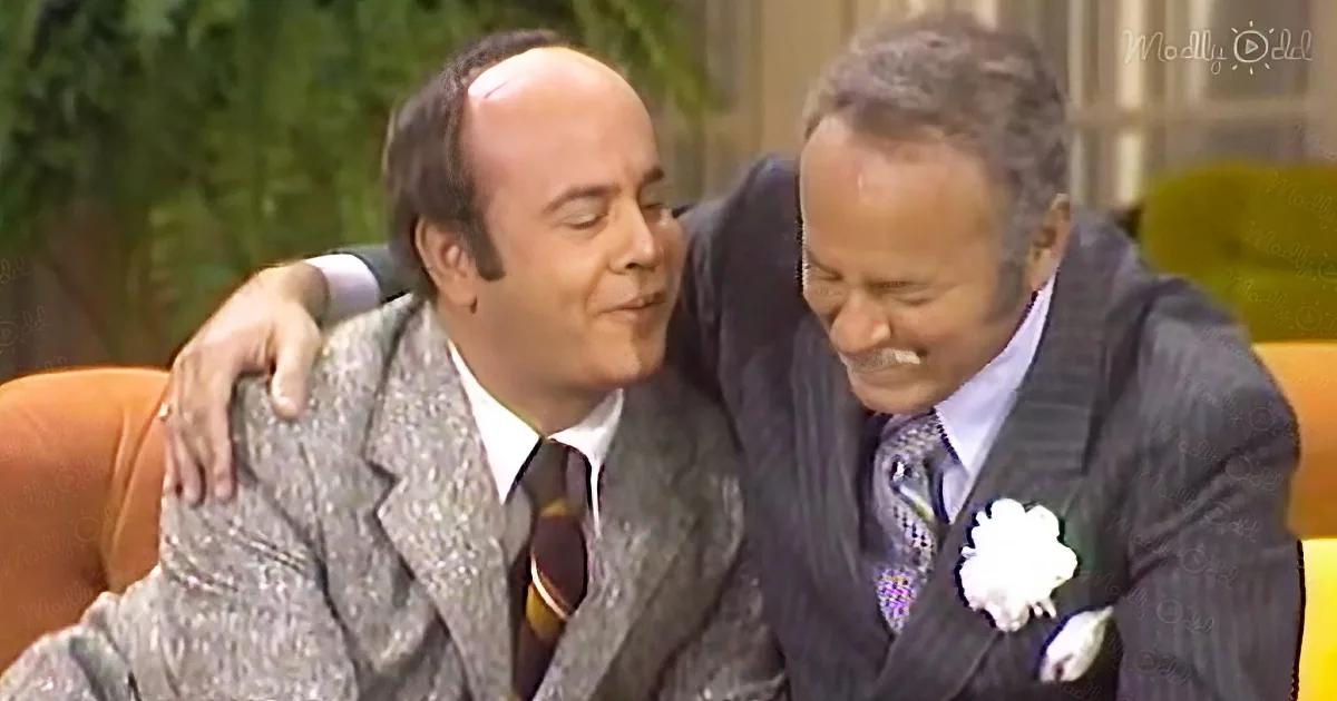 Two men in suits share a warm embrace, one wearing a white flower on his lapel.