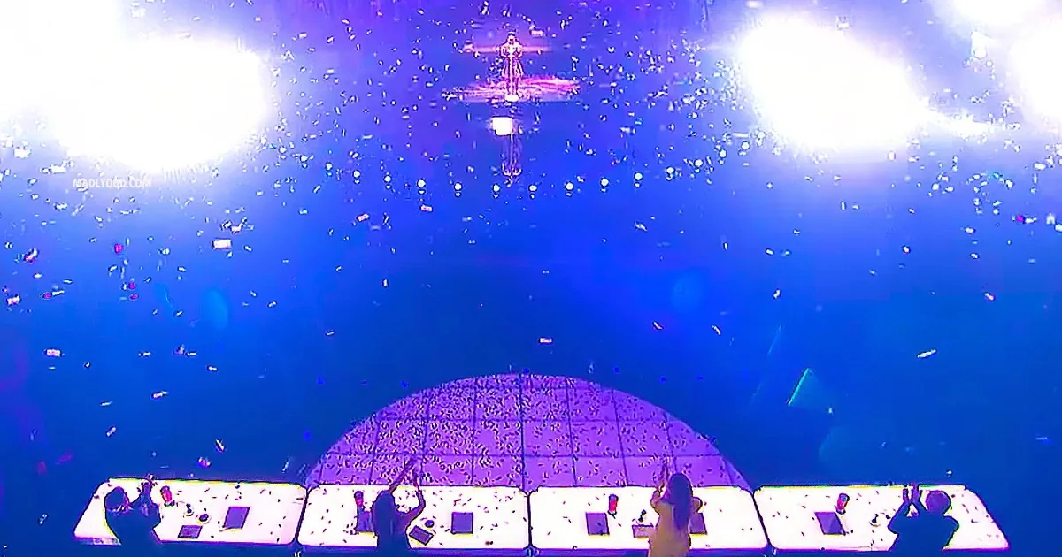 A performer on stage with bright lights and confetti falling, creating a vibrant concert atmosphere.