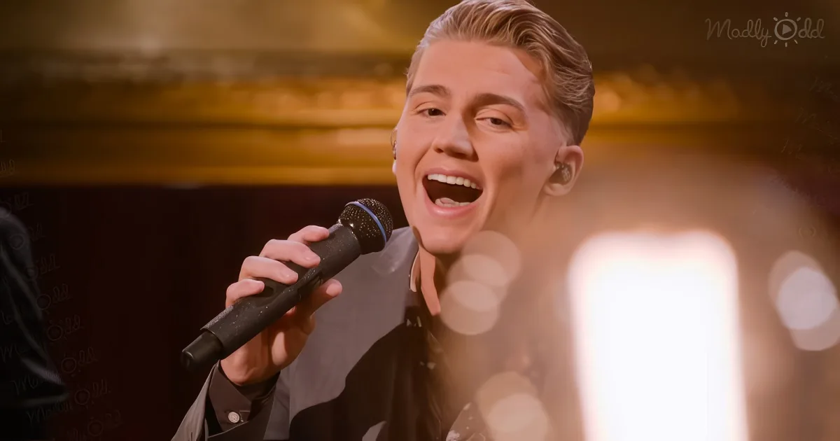 A person in a suit sings into a microphone, with a blurred background and bokeh effect.
