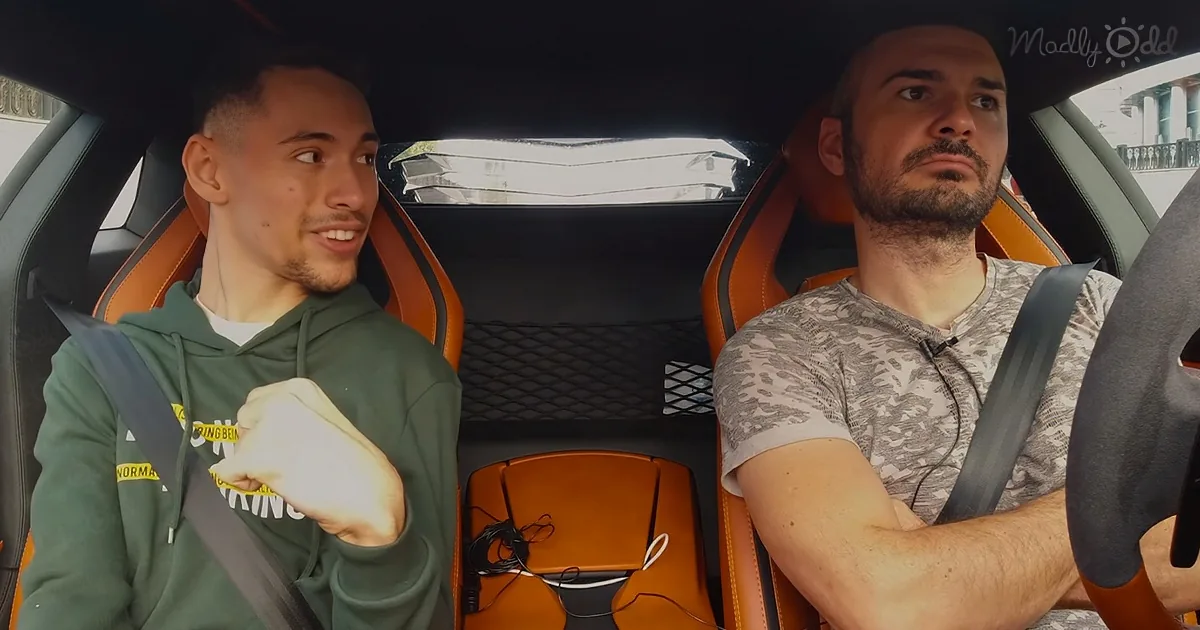 Two men are in a car, one in a green hoodie gesturing, the other in a camo shirt driving.
