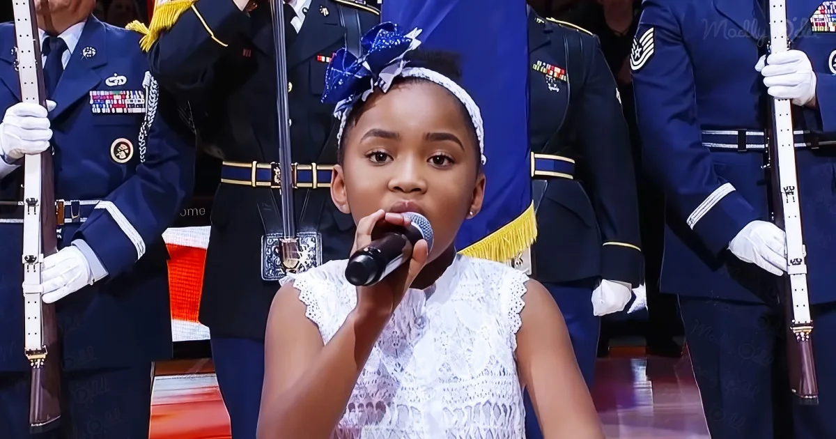 A young girl in a white dress sings into a microphone, surrounded by uniformed military personnel holding rifles.